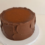 Chocolate frosted cake on a white plate with a beige background